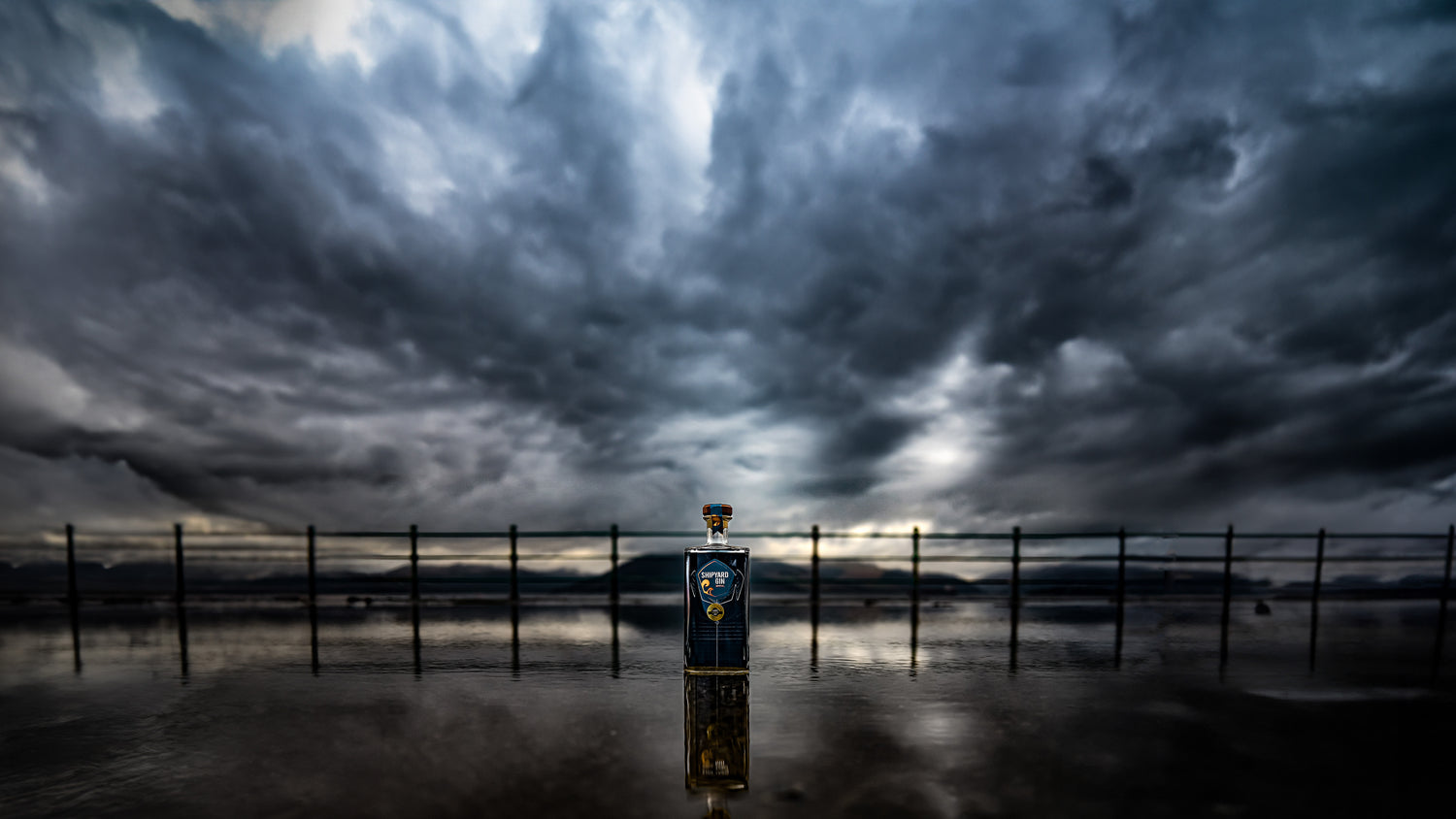 Bottle of Shipyard Gin against a dramatic sky with clouds.